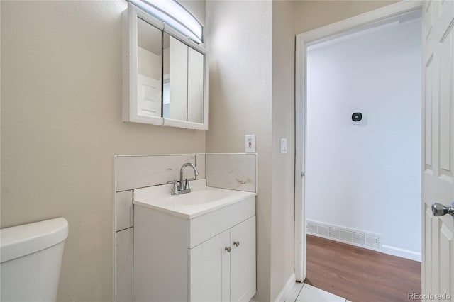 half bathroom featuring visible vents, toilet, vanity, wood finished floors, and baseboards