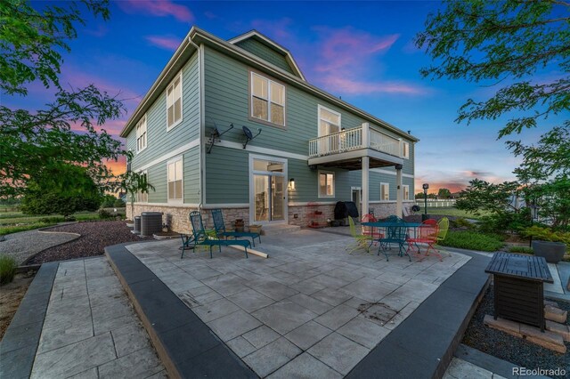 881 Kirby Ct, Watkins, CO 80137 - back of house at dusk featuring stone siding, a patio, and a balcony