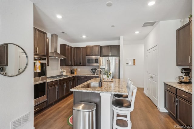 27593 E 1st Pl, Aurora, CO 80018 - kitchen featuring wall chimney exhaust hood, a sink, appliances with stainless steel finishes, wood finished floors, and dark brown cabinets