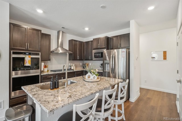 27593 E 1st Pl, Aurora, CO 80018 - kitchen with wall chimney range hood, stainless steel appliances, dark brown cabinets, a breakfast bar area, and a sink