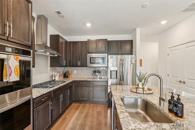 27593 E 1st Pl, Aurora, CO 80018 - kitchen featuring a sink, stainless steel appliances, wall chimney range hood, light wood-style floors, and decorative backsplash