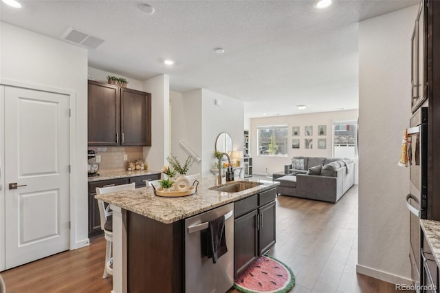 27593 E 1st Pl, Aurora, CO 80018 - kitchen featuring stainless steel dishwasher, a sink, wood finished floors, dark brown cabinetry, and tasteful backsplash