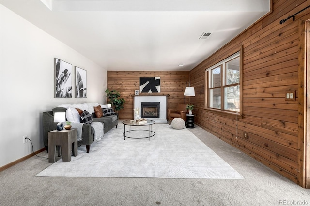 living room with visible vents, a fireplace with raised hearth, wood walls, and carpet floors