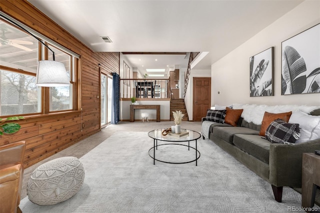 carpeted living room featuring stairs, wooden walls, and visible vents