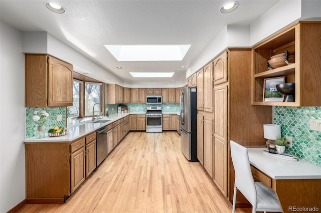 kitchen with a sink, appliances with stainless steel finishes, a skylight, and light wood finished floors