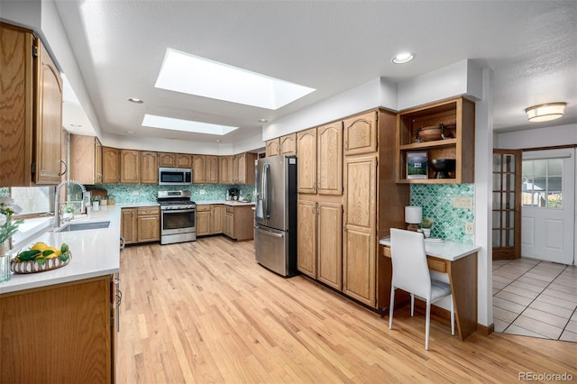 kitchen featuring a sink, backsplash, appliances with stainless steel finishes, a skylight, and light countertops