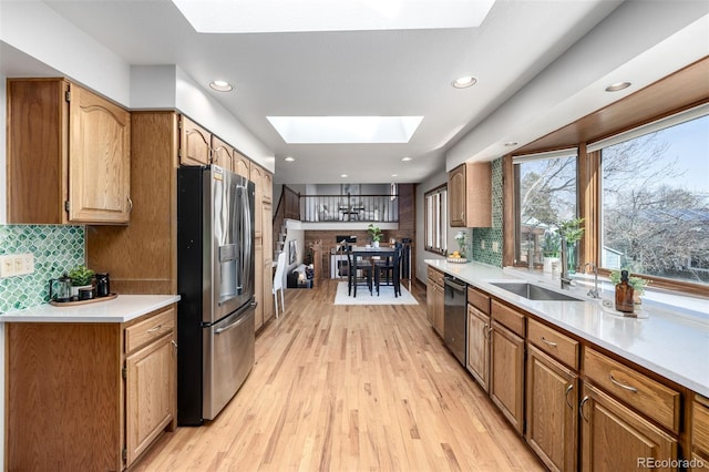 kitchen featuring a skylight, light wood-style flooring, stainless steel appliances, decorative backsplash, and light countertops