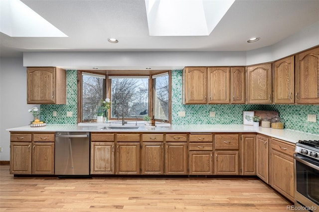 kitchen featuring brown cabinets, appliances with stainless steel finishes, a skylight, light wood-style flooring, and a sink