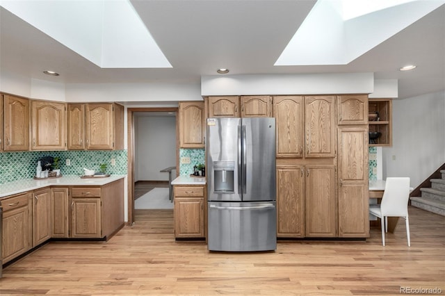 kitchen featuring light wood-type flooring, a skylight, decorative backsplash, light countertops, and stainless steel fridge