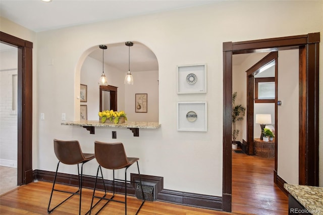 kitchen featuring pendant lighting, light stone counters, a kitchen breakfast bar, and hardwood / wood-style floors