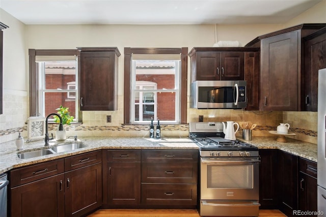 kitchen with backsplash, sink, light stone counters, dark brown cabinetry, and stainless steel appliances