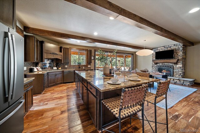 8090 S Homesteader Dr, Morrison, CO 80465 - kitchen featuring stainless steel appliances, a kitchen bar, beam ceiling, dark brown cabinets, and light wood-style flooring