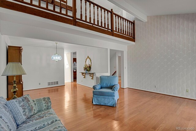 living room with beam ceiling, light wood-type flooring, and a notable chandelier