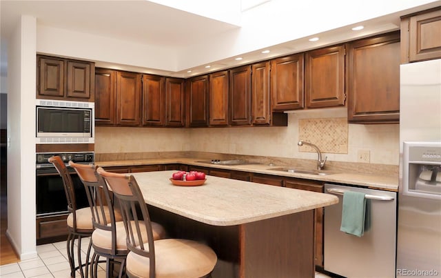 kitchen featuring sink, a kitchen island, a breakfast bar, light tile patterned floors, and appliances with stainless steel finishes