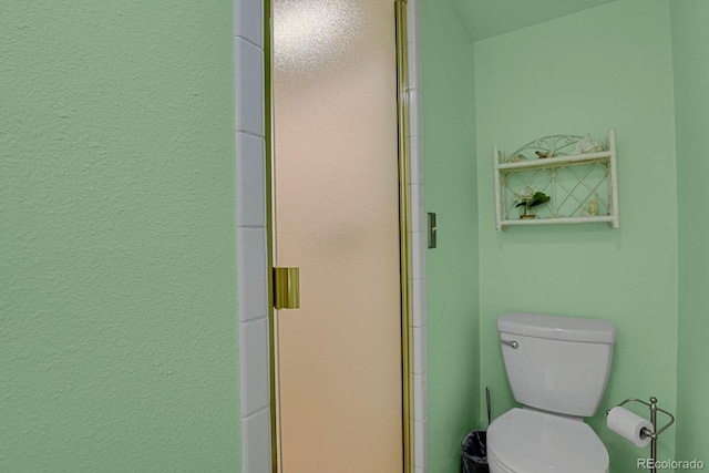 bathroom featuring a shower with door and toilet