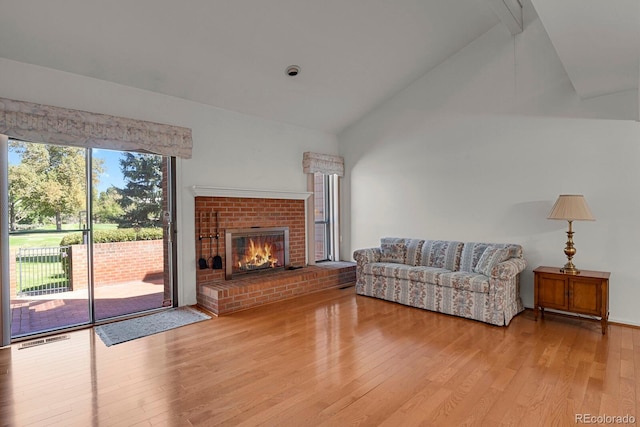 living room featuring light wood-type flooring, a brick fireplace, and lofted ceiling