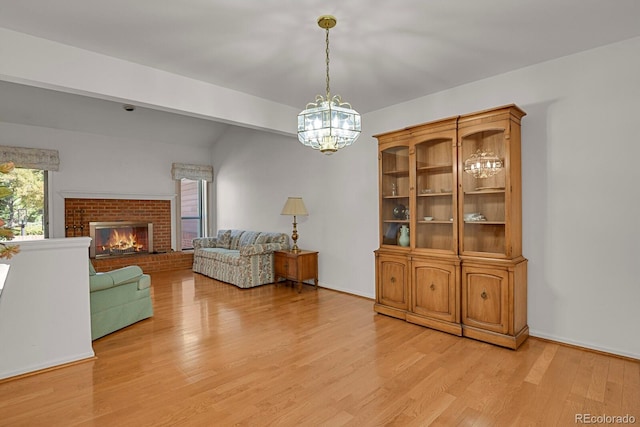 living room with light hardwood / wood-style flooring, a notable chandelier, and a brick fireplace