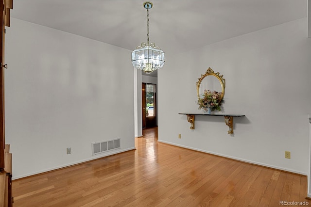 spare room featuring light wood-type flooring and an inviting chandelier