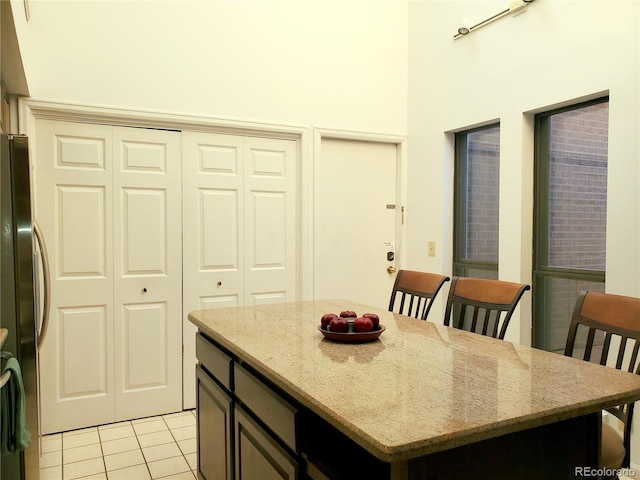 kitchen featuring a center island, light tile patterned flooring, light stone countertops, and stainless steel refrigerator