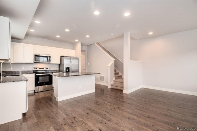 kitchen with a kitchen island, white cabinets, a sink, dark stone countertops, and appliances with stainless steel finishes
