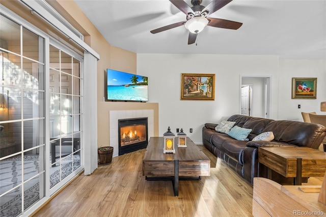 living room with ceiling fan, light hardwood / wood-style flooring, and a tiled fireplace