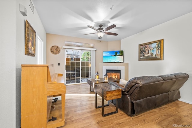 living room with hardwood / wood-style flooring, ceiling fan, and a tiled fireplace