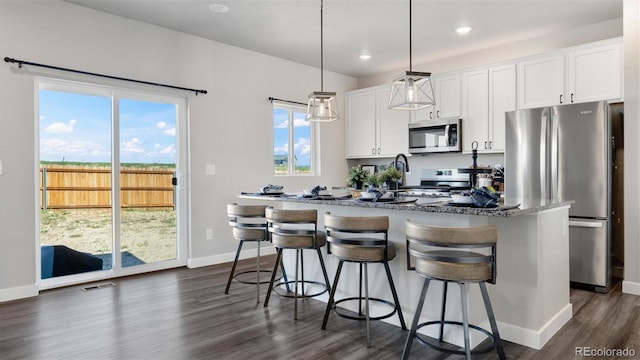 kitchen featuring appliances with stainless steel finishes, a breakfast bar, a center island with sink, white cabinetry, and hanging light fixtures