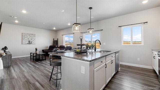 kitchen featuring dark stone counters, a center island with sink, hanging light fixtures, sink, and white cabinetry