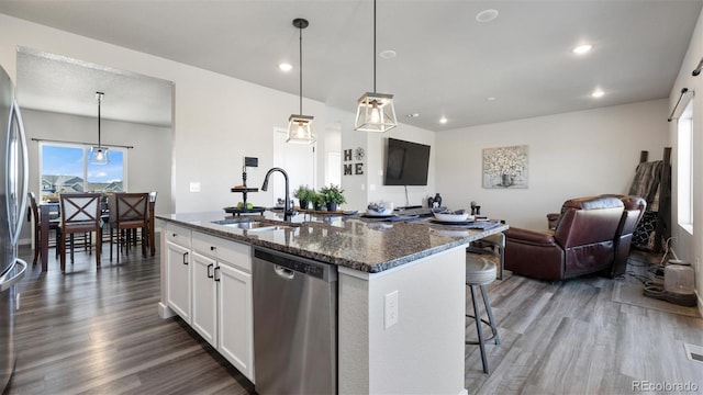 kitchen with stainless steel dishwasher, dark stone counters, decorative light fixtures, a kitchen island with sink, and white cabinets