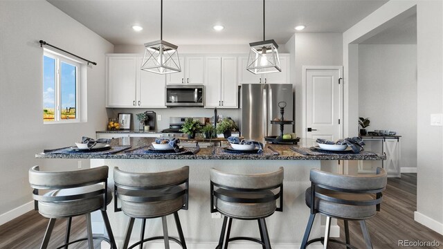 kitchen featuring a kitchen breakfast bar, white cabinetry, hanging light fixtures, and stainless steel appliances