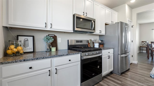 kitchen with stainless steel appliances, white cabinetry, hardwood / wood-style flooring, and dark stone countertops