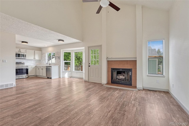 unfurnished living room featuring a textured ceiling, ceiling fan, sink, high vaulted ceiling, and light hardwood / wood-style flooring