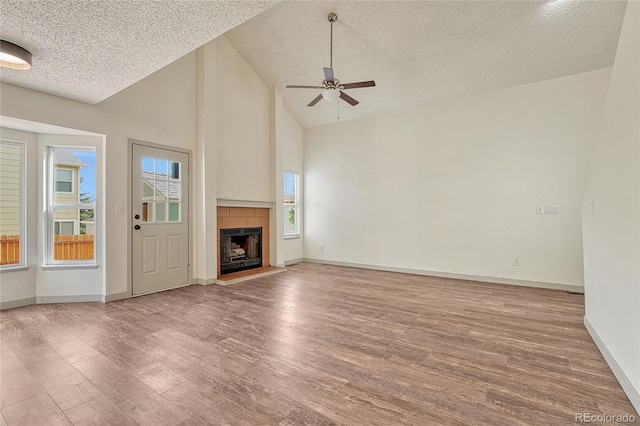 unfurnished living room featuring a textured ceiling, ceiling fan, high vaulted ceiling, light hardwood / wood-style floors, and a tiled fireplace