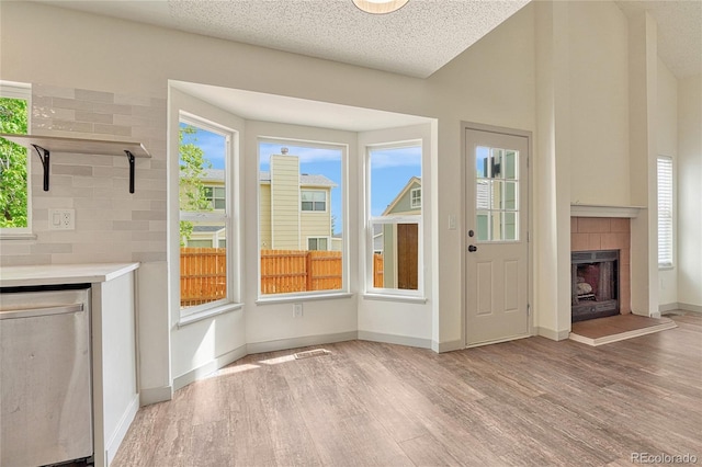 doorway to outside with a tiled fireplace, a textured ceiling, and light hardwood / wood-style flooring