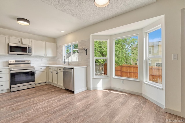 kitchen with sink, decorative backsplash, light wood-type flooring, appliances with stainless steel finishes, and white cabinetry