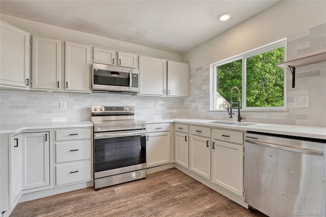 kitchen with hardwood / wood-style floors, appliances with stainless steel finishes, white cabinetry, and sink