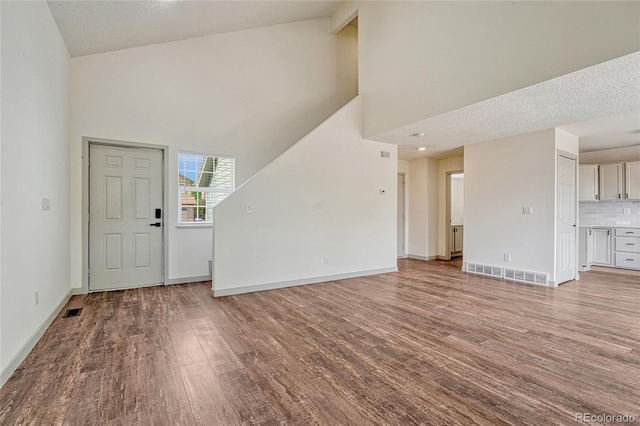 foyer featuring high vaulted ceiling, wood-type flooring, and a textured ceiling