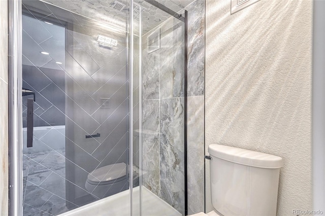 bathroom featuring a shower with shower door and toilet