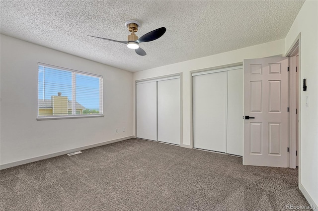 unfurnished bedroom featuring two closets, ceiling fan, carpet floors, and a textured ceiling