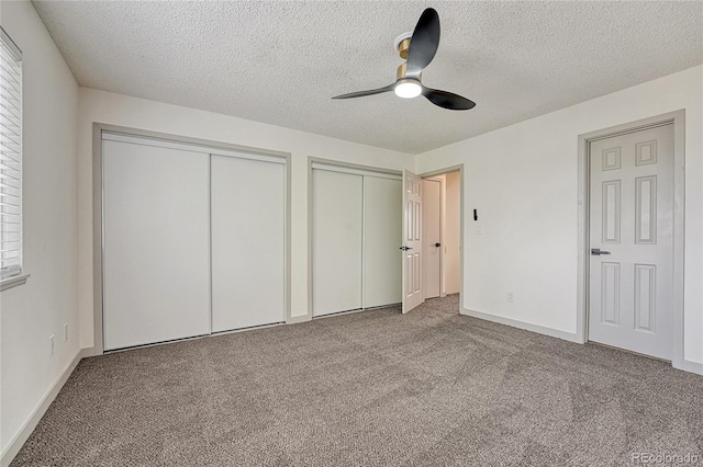 unfurnished bedroom featuring carpet, ceiling fan, a textured ceiling, and two closets