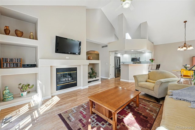 2252 S Yosemite Cir, Denver, CO 80231 - living area with visible vents, a glass covered fireplace, high vaulted ceiling, light wood-style flooring, and ceiling fan with notable chandelier