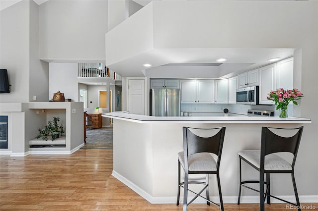kitchen with a high ceiling, appliances with stainless steel finishes, light wood-style flooring, a peninsula, and a kitchen bar