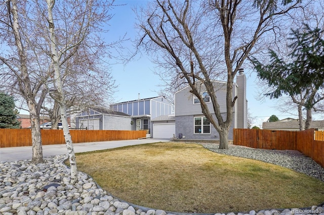 rear view of house featuring driveway, a chimney, an attached garage, fence, and brick siding