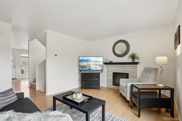 living room featuring light wood-type flooring, baseboards, stairway, and a tile fireplace