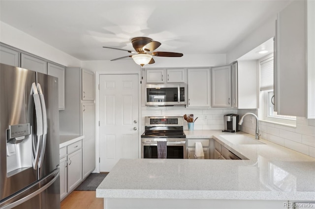 kitchen featuring light stone counters, gray cabinets, decorative backsplash, appliances with stainless steel finishes, and a sink