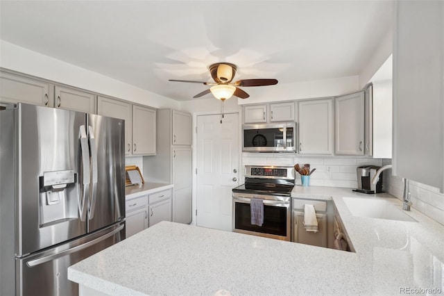 kitchen with decorative backsplash, appliances with stainless steel finishes, a peninsula, gray cabinets, and a sink