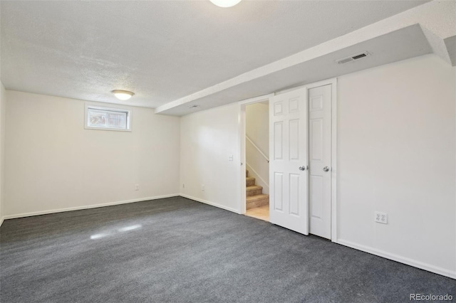 below grade area featuring baseboards, visible vents, stairway, dark colored carpet, and a textured ceiling