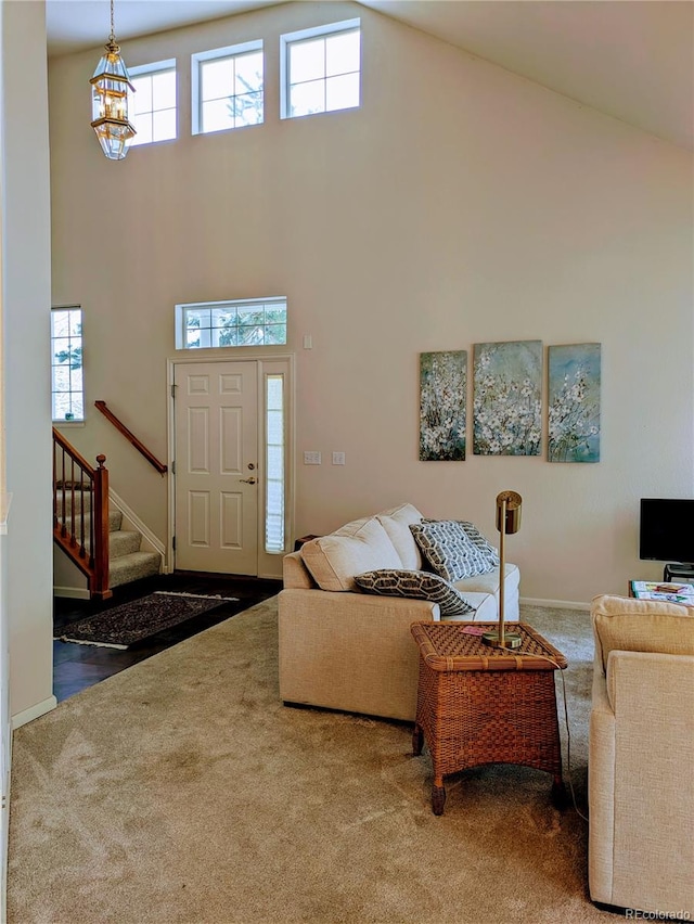 carpeted living area featuring stairs, high vaulted ceiling, a chandelier, and baseboards