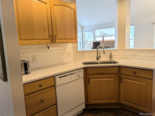 kitchen featuring light stone counters, white dishwasher, a sink, and decorative backsplash