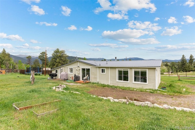 rear view of property with a lawn, a mountain view, and a trampoline